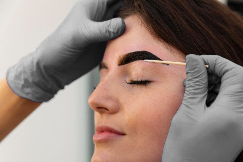 Esthetician designing woman's eyebrows with henna or tint 